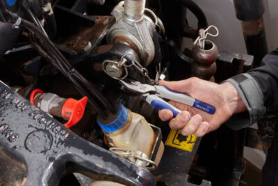 Mechanic inspecting a racing vehicle's engine with a digital tool, focusing on performance and maintenance for Grand Prix Racewear.