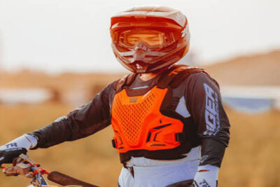 Motocross rider wearing Grand Prix Racewear with orange chest protector and full-face helmet on dirt track.