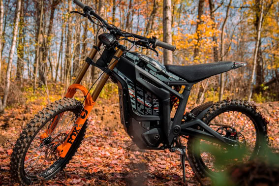 Electric mountain bike with orange suspension forks and black frame in a forest during autumn.