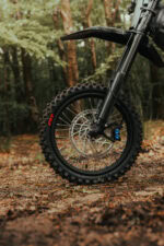 Close-up of a mountain bike front wheel with disc brake on a forest trail.