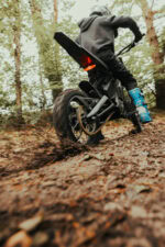 Child riding a dirt bike through a forest trail, wearing a helmet and protective gear.