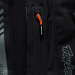 Close-up of Troy Lee Designs SCOUT GP PRO Mono Bottoms racing gear with black fabric and orange zipper pull.